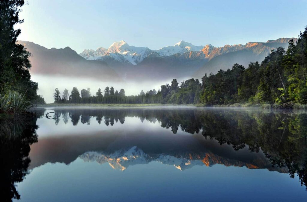 Jezero se stromy a horami v pozadí Jezero se stromy a horami v pozadí