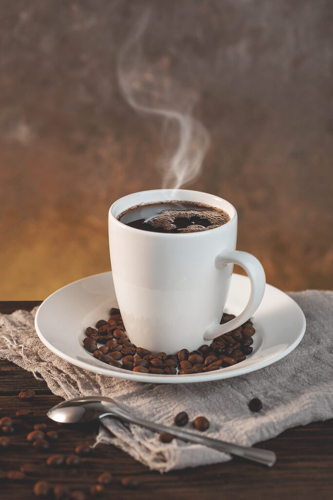 A cup of coffee on a plate with beans and a spoon A cup of coffee on a plate with beans and a spoon